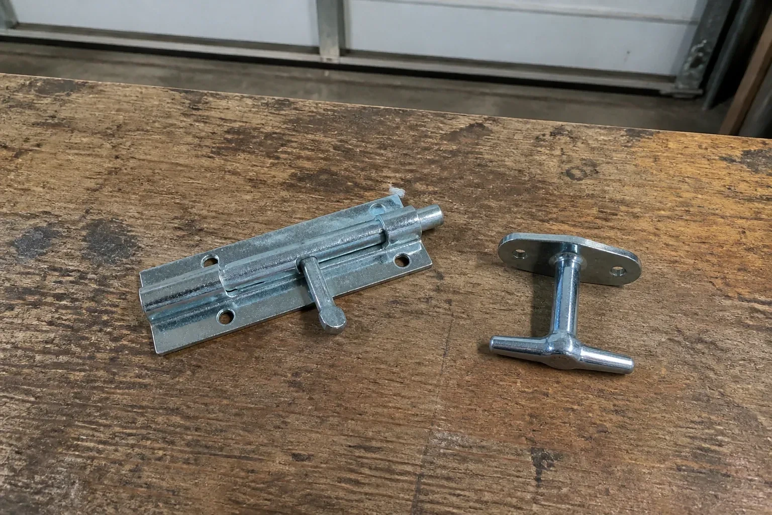 Detached slide bolt and T-handle on a wooden garage workbench. — Garage Door Manual Lock Repair, Springwater