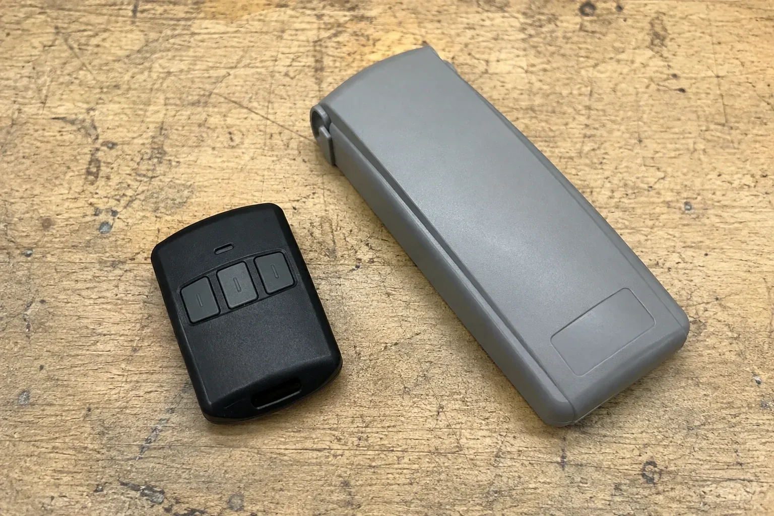 Three-button remote beside a closed grey keypad cover on a workbench. — Garage Door Remote and Keypad Programming, Springwater