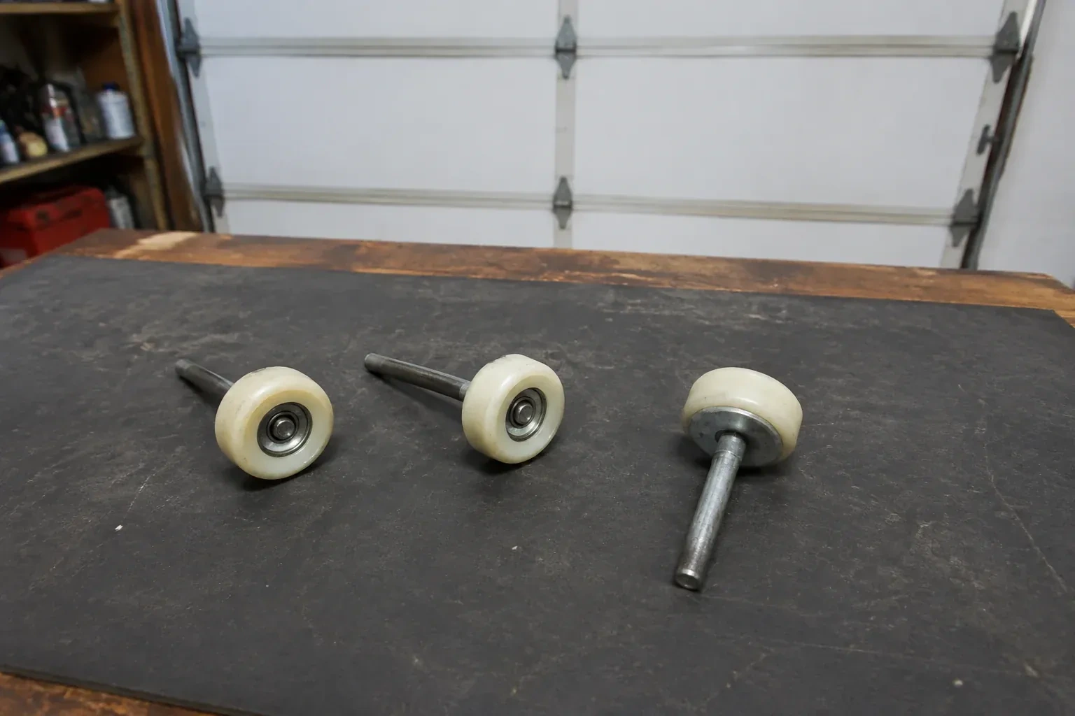 Three detached nylon-wheel garage door rollers with steel stems on a work mat. — Garage Door Roller Replacement, Springwater